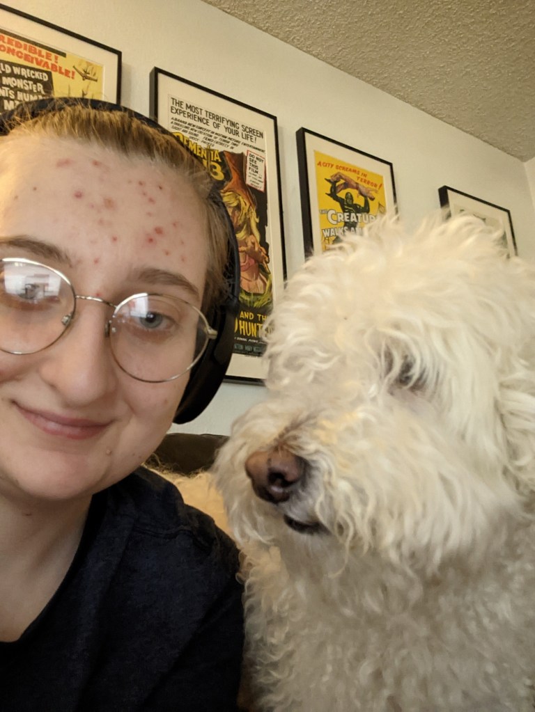 Landis, a white demiguy wearing noise canceling headphones and glasses, smiles lightly at the camera. Next to him is a white poodle named Jack who is looking off into the distance. You can barely see his eyes because his adorable eyebrows hang over them akin to curtains.